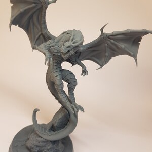 May include: A gray 3D printed dragon figurine with wings outstretched and a curled tail. The dragon is perched on a rock base.