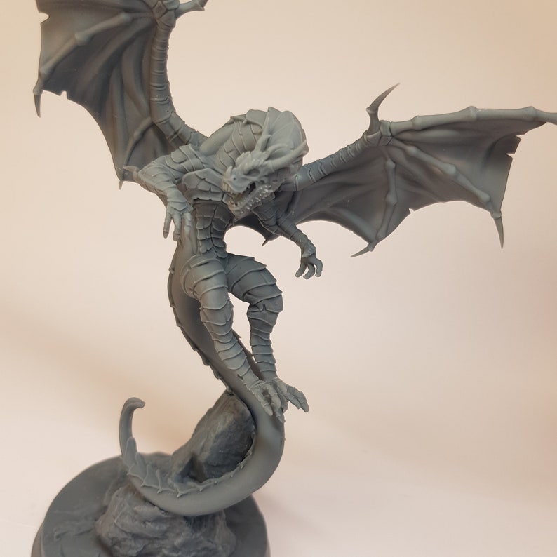 May include: A gray 3D printed dragon figurine with wings outstretched and a curled tail. The dragon is perched on a rock base.