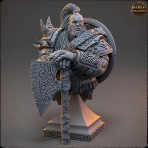 May include: A grey painted bust of a warrior with a large axe and shield. The warrior is wearing a horned helmet and a fur cloak. The bust is on a grey base.