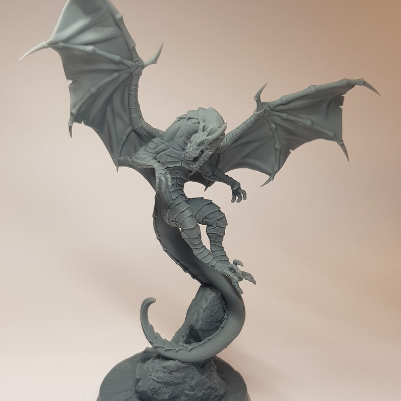 May include: A gray, detailed dragon figurine with wings spread wide, perched on a rock base. The dragon's tail curls around the rock, creating a dynamic pose.