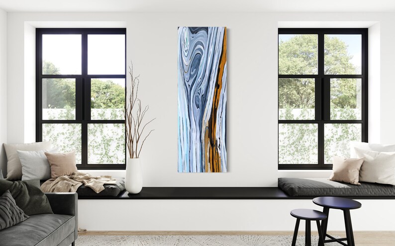 May include: Abstract painting with swirling blue, white, and orange colors. The painting has a vertical format and is framed in a modern, minimalist style.