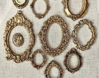 May include: A collection of nine ornate gold-toned picture frames of various sizes and shapes, arranged on a beige textured background.
