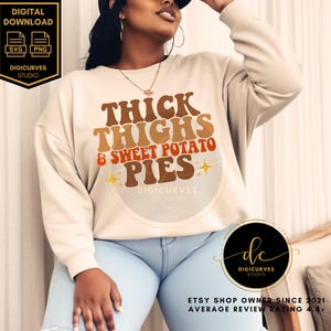 May include: A white sweatshirt with the text "Thick Thighs & Sweet Potato Pies" in a retro font with orange, brown, and yellow accents. The text is surrounded by a circle with stars.
