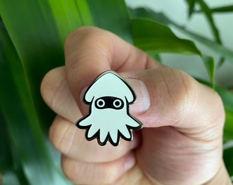 May include: A white enamel pin with a black outline of a squid wearing a mask. The squid has two large eyes and a small mouth.