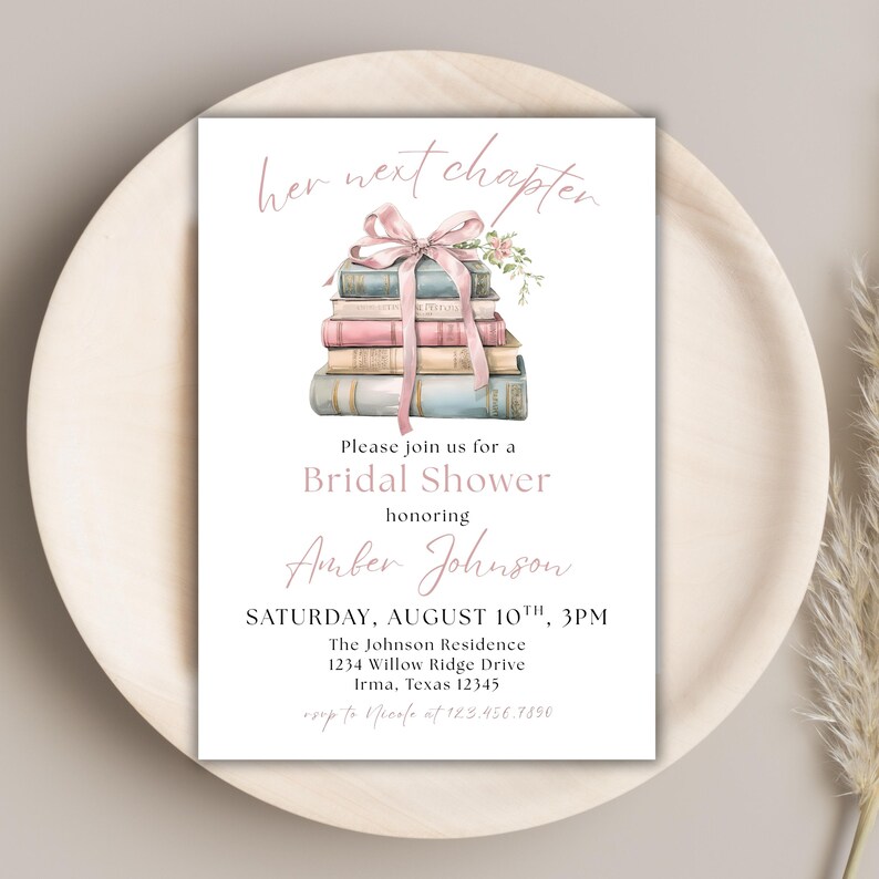 May include: A white bridal shower invitation with a pink ribbon and a stack of books. The text reads "her next chapter" and "Please join us for a Bridal Shower honoring Amber Johnson". The date and time of the shower are listed as "SATURDAY, AUGUST 10TH, 3PM". The location is listed as "The Johnson Residence, 1234 Willow Ridge Drive, Irma, Texas 12345".