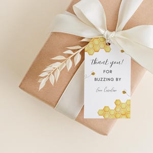 Könnte beinhalten: Ein weißes Dankeschön-Etikett mit einem Wabenmuster und Bienen. Der Text lautet "Vielen Dank! Für den Besuch Liebe Caroline".