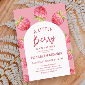 Puede incluir: Una invitación de baby shower rosa con un círculo blanco y el texto "A Little Berry Is On The Way" con el nombre "Elizabeth Morris" y la fecha "Sábado, 30 de agosto, 2 PM". La invitación tiene un fondo rosa con ilustraciones de acuarela de frambuesas.