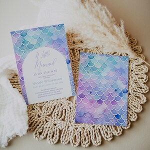 May include: A baby shower invitation with a mermaid theme. The invitation is decorated with a watercolor design of purple, blue, and green mermaid scales. The text on the invitation reads "A Little Mermaid is on the Way" and includes the name "Nicole Williamson" and the date "Saturday June 12th 3PM".