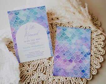 Peut inclure: Une invitation à une fête prénatale sur le thème de la sirène. L'invitation est décorée d'un motif aquarelle d'écailles de sirène violettes, bleues et vertes. Le texte de l'invitation indique "A Little Mermaid is on the Way" et comprend le nom "Nicole Williamson" et la date "Saturday June 12th 3PM".