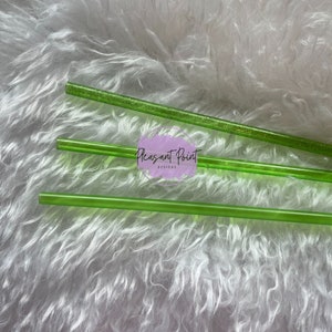 Puede incluir: Varias pajitas transparentes de color verde brillante est&aacute;n dispuestas sobre una superficie blanca y esponjosa. Una pajita tiene purpurina incrustada. El texto "Pleasant Point Designs" es visible en la imagen.