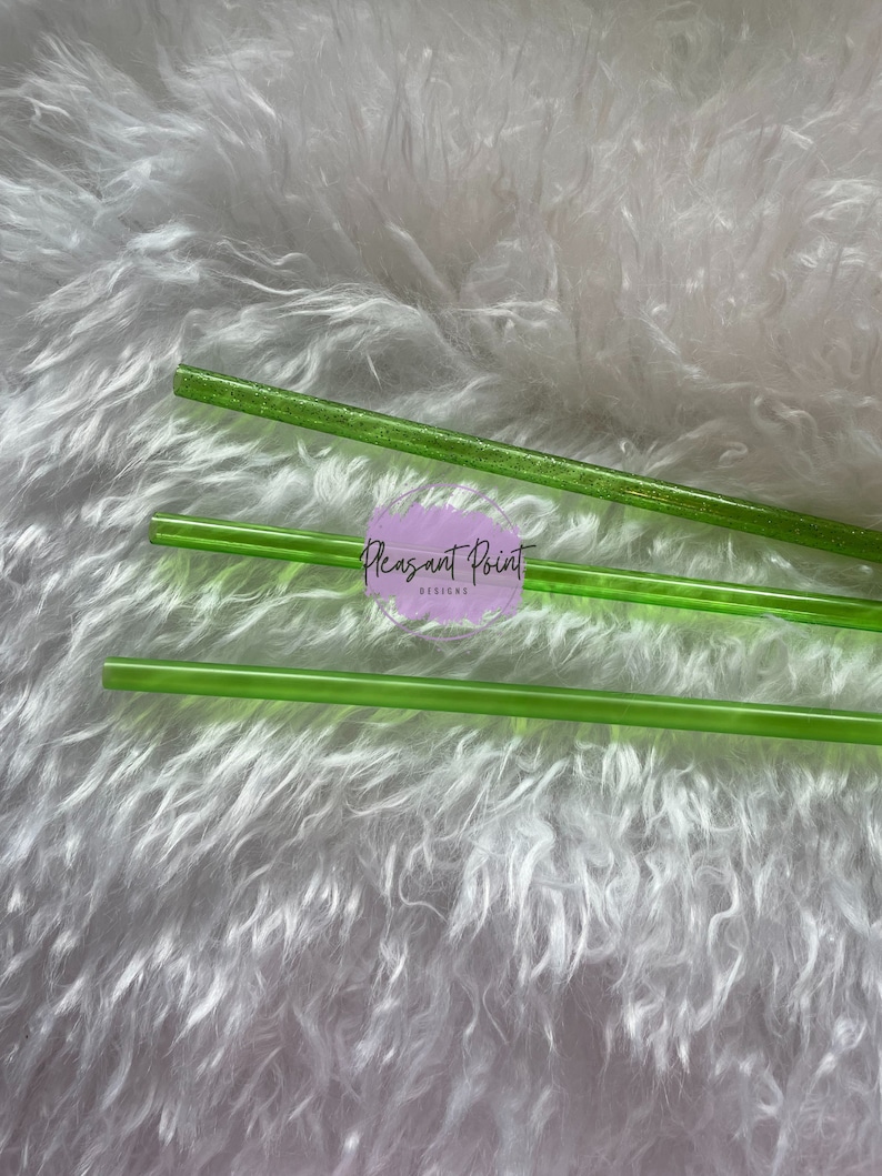 Puede incluir: Varias pajitas transparentes de color verde brillante est&aacute;n dispuestas sobre una superficie blanca y esponjosa. Una pajita tiene purpurina incrustada. El texto "Pleasant Point Designs" es visible en la imagen.