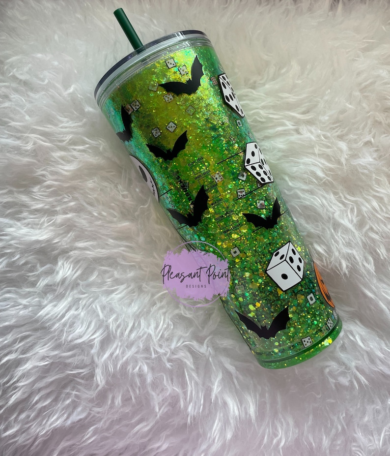 Puede incluir: Un vaso verde con purpurina y calcoman&iacute;as de murci&eacute;lagos y dados negros. El vaso tiene una pajita verde y una tapa negra. El vaso est&aacute; decorado con un tema de Halloween. El vaso es de pl&aacute;stico.