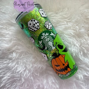 Puede incluir: Un vaso verde con purpurina, dados blancos, un logotipo de Starbucks y un dise&ntilde;o de personaje de dibujos animados. El vaso tiene una tapa negra y una pajita morada. El texto "Pleasant Point Designs" es visible.