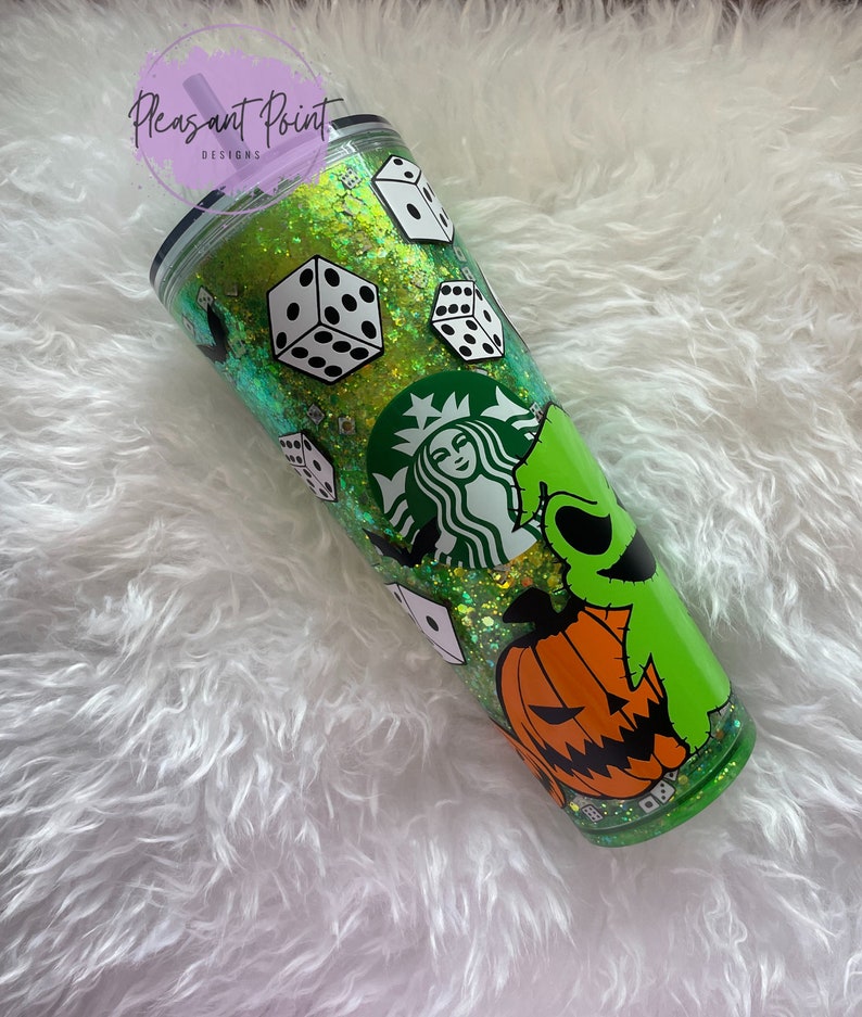 Puede incluir: Un vaso verde con purpurina, dados blancos, un logotipo de Starbucks y un dise&ntilde;o de personaje de dibujos animados. El vaso tiene una tapa negra y una pajita morada. El texto "Pleasant Point Designs" es visible.
