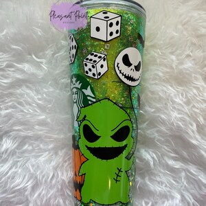 Puede incluir: Un vaso transparente de doble pared con un interior de purpurina verde, con calcoman&iacute;as de personajes de Pesadilla antes de Navidad. Incluye im&aacute;genes de dados, Jack Skellington y Oogie Boogie. El vaso tiene una pajita verde y el texto "Pleasant Point Designs".