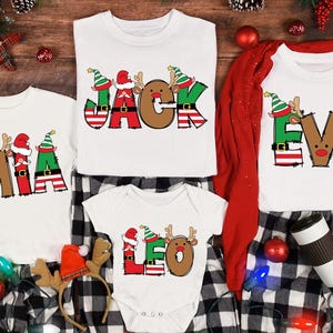 May include: White Christmas-themed family pajamas with personalized names. The shirts feature names like "Jack", "Mia", "Eva", and "Leo" in festive colors. The pajamas are paired with black and white checkered pants, and holiday decorations.