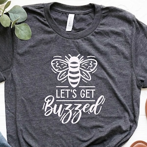 May include: A dark gray t-shirt with a white bee graphic and the text "Let's Get Buzzed".