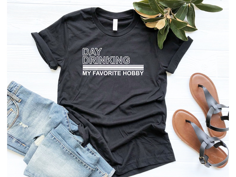 K&ouml;nnte beinhalten: Schwarzes T-Shirt mit wei&szlig;em Text, der "Day Drinking My Favorite Hobby" lautet.