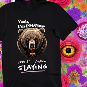 Könnte beinhalten: Schwarzes T-Shirt mit einem Bären-Motiv und dem Text "Yeah, I'm PMS'ing. Pretty Manic Slaying" in Weiß und Rosa.