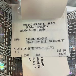 Puede incluir: Primer plano de una prenda con lentejuelas y abalorios plateados. Una etiqueta de precio de Robinsons May, Glendale Galleria, Glendale, California, est&aacute; adjunta. La etiqueta incluye detalles del art&iacute;culo y un precio.