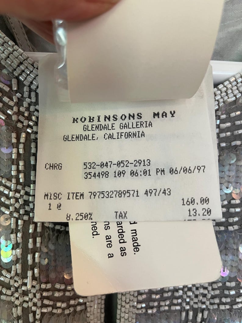 Puede incluir: Primer plano de una prenda con lentejuelas y abalorios plateados. Una etiqueta de precio de Robinsons May, Glendale Galleria, Glendale, California, est&aacute; adjunta. La etiqueta incluye detalles del art&iacute;culo y un precio.