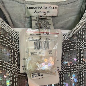 Puede incluir: Chaqueta con cuentas Adrianna Papell Evening plateada, con un patr&oacute;n de cuadr&iacute;cula de lentejuelas y cuentas. La etiqueta dice "Beaded Jacket" y "XL". La chaqueta tiene una capa de seda y forro de ray&oacute;n. Se adjunta una peque&ntilde;a bolsa de lentejuelas.