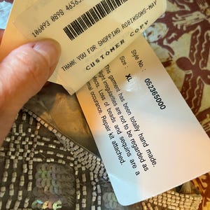 Puede incluir: Primer plano de una prenda hecha a mano con detalles de cuentas y lentejuelas. El dise&ntilde;o presenta un patr&oacute;n de cuadr&iacute;cula con lentejuelas iridiscentes. Las etiquetas adjuntas dicen "GRACIAS POR COMPRAR EN ROBINSONS-MAY" y "Talla: XL".