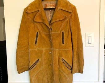 May include: A brown suede jacket with a collared neckline, long sleeves, and a button closure. The jacket has a label that reads "The Tannery".