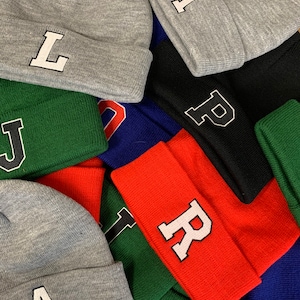May include: A pile of colourful knitted beanies with large felt letters on the front. The letters spell out the word "JUSTRIAL".