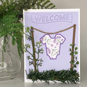 Baby shower.Nouveau bébé. Carte de voeux violette. Intérieur vierge pour votre message de bienvenue. Fanions sur la corde à linge avec des fleurs. Prêt à être expédié !
