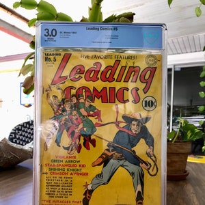 Może przedstawiać: Okładka komiksu z epoki przedstawiająca grupę superbohaterów w akcji. Okładka jest żółta z czerwonymi i niebieskimi akcentami. Tytuł komiksu to "Leading Comics", a numer wydania to 5. Okładka zawiera tekst "Five Favorite Features!" i wymienia imiona superbohaterów: Vigilante, Green Arrow, Star-Spangled Kid, Shining Knight i Crimson Avenger.