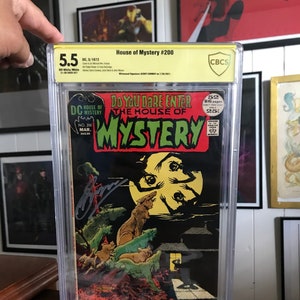 Puede incluir: Un cómic clasificado en una caja de plástico. El cómic se titula "House of Mystery #200" y presenta una ilustración en blanco y negro de una criatura con múltiples ojos. El cómic está clasificado con un 5,5 por CBCS.