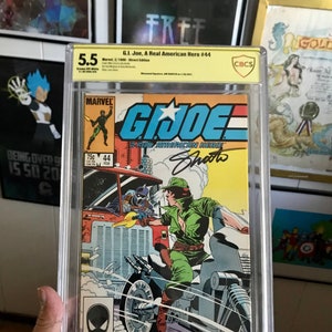 Puede incluir: Un cómic calificado en una caja de plástico. La portada del cómic presenta una ilustración colorida de un personaje de la franquicia G.I. Joe, conduciendo una motocicleta. El cómic se titula "G.I. Joe, A Real American Hero" y el número de la edición es 44. El cómic está calificado con 5.5 por CBCS.