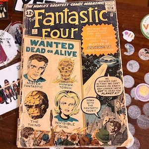 Può includere: Un fumetto vintage "I Fantastici Quattro" con la copertina che presenta i personaggi Mister Fantastic, Torcia Umana, La Cosa e Ragazza Invisibile. Il fumetto è invecchiato e usurato.