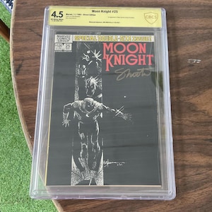 Puede incluir: Un cómic Moon Knight #25 calificado. La portada presenta una ilustración en blanco y negro del personaje Moon Knight. El cómic está encerrado en un soporte protector transparente con una calificación CBCS de 4.5.