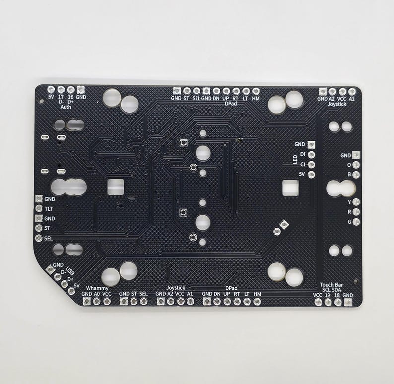 Puede incluir: Una placa de circuito impreso negra con varios componentes, incluyendo un joystick, una barra t&aacute;ctil, un D-pad y una barra Whammy. La placa tiene etiquetas para GND, 5V, VCC, A1, A2, SCL, SDA, ST, SEL, ON, UP, RT, LT, HM, TLT, D, CI, SV, B, Y, R, G y Auth.