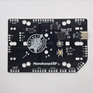 Puede incluir: Una placa de circuito impreso negra con el texto "Monoboard RP 2.2" impreso en ella. La placa tiene una variedad de componentes, incluyendo un joystick, una barra t&aacute;ctil, un interruptor de inclinaci&oacute;n y un bot&oacute;n etiquetado como "BOOT". La placa tambi&eacute;n tiene un conector USB-C y un conector micro-HDMI.