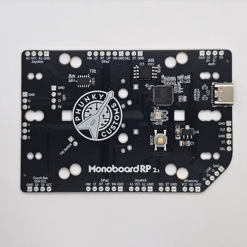 Puede incluir: Una placa de circuito impreso negra con el texto "Monoboard RP 2.2" impreso en ella. La placa tiene una variedad de componentes, incluyendo un joystick, una barra t&aacute;ctil, un interruptor de inclinaci&oacute;n y un bot&oacute;n etiquetado como "BOOT". La placa tambi&eacute;n tiene un conector USB-C y un conector micro-HDMI.