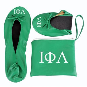 May include: Green foldable ballet flats with a matching carrying case. The flats and case feature white Greek letters. The flats have a bow detail and a black sole. The case has a white zipper.