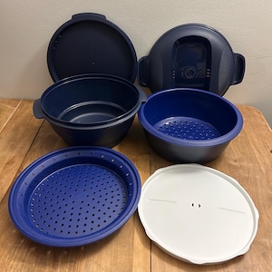 May include: A selection of navy blue and white kitchenware items, including bowls, lids, and a perforated insert. The pieces are displayed on a wooden surface, highlighting their different forms and dimensions. The set is likely intended for food preparation and storage.
