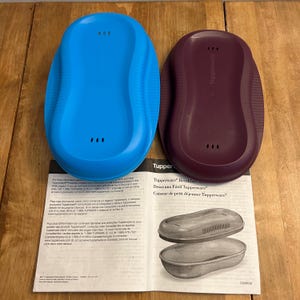 May include: Two Tupperware Breakfast Maker containers in blue and burgundy, each with three small holes on the top. An instruction sheet is below, with the Tupperware logo and product name.