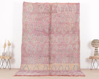 May include: A pink and cream Moroccan rug with a diamond pattern. The rug has a fringe border and is made of wool.