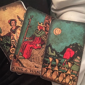 Può includere: Tre carte dei tarocchi, Re di Bastoni, Otto di Coppe e la Luna. La carta del Re di Bastoni presenta un re seduto su un trono con un bastone in mano. La carta dell'Otto di Coppe presenta otto coppe su un sentiero con una figura che si allontana da esse. La carta della Luna presenta una luna crescente nel cielo e una figura che cammina in primo piano.