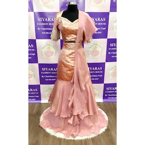 Puede incluir: Un atuendo de novia indio rosa y dorado con una falda con volantes y una blusa a juego. El atuendo está sobre una superficie de piel blanca.