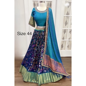May include: A blue and green patterned skirt with a matching blue blouse and a gold embroidered border. The skirt has a floral print and the blouse has a round neckline. The outfit is complete with a matching blue dupatta with a gold border. Size 44.
