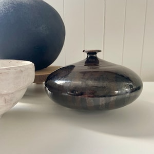 May include: A dark brown ceramic vase with a glossy finish. The vase has a wide, round base and a narrow neck.