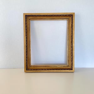 May include: A rectangular picture frame with a metallic gold finish and a dark brown inner border. The frame features a multi-layered profile with a rope-like texture detail along the inner edge, providing a structured and ornate appearance.