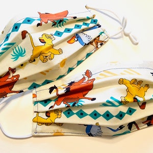 May include: Two white face masks with a repeating pattern of characters from the Lion King movie. The characters include Simba, Pumbaa, and Zazu. The masks have white elastic ear loops.