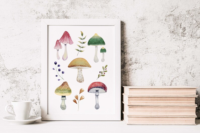 May include: A framed watercolor print featuring various colorful mushrooms and foliage. The artwork includes mushrooms with red, green, and brown caps, along with sprigs of leaves and berries. The print is displayed on a white surface.