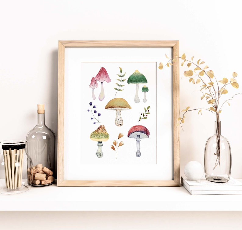 May include: A framed watercolor print featuring various colorful mushrooms and foliage. The mushrooms have red, green, yellow, and brown caps with white stems. The artwork is displayed on a white shelf with decorative items.